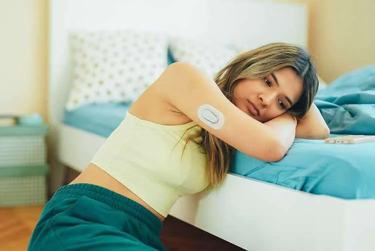 A young, slim woman is wearing a small sensor on the back of her arm to monitor her blood sugar levels
