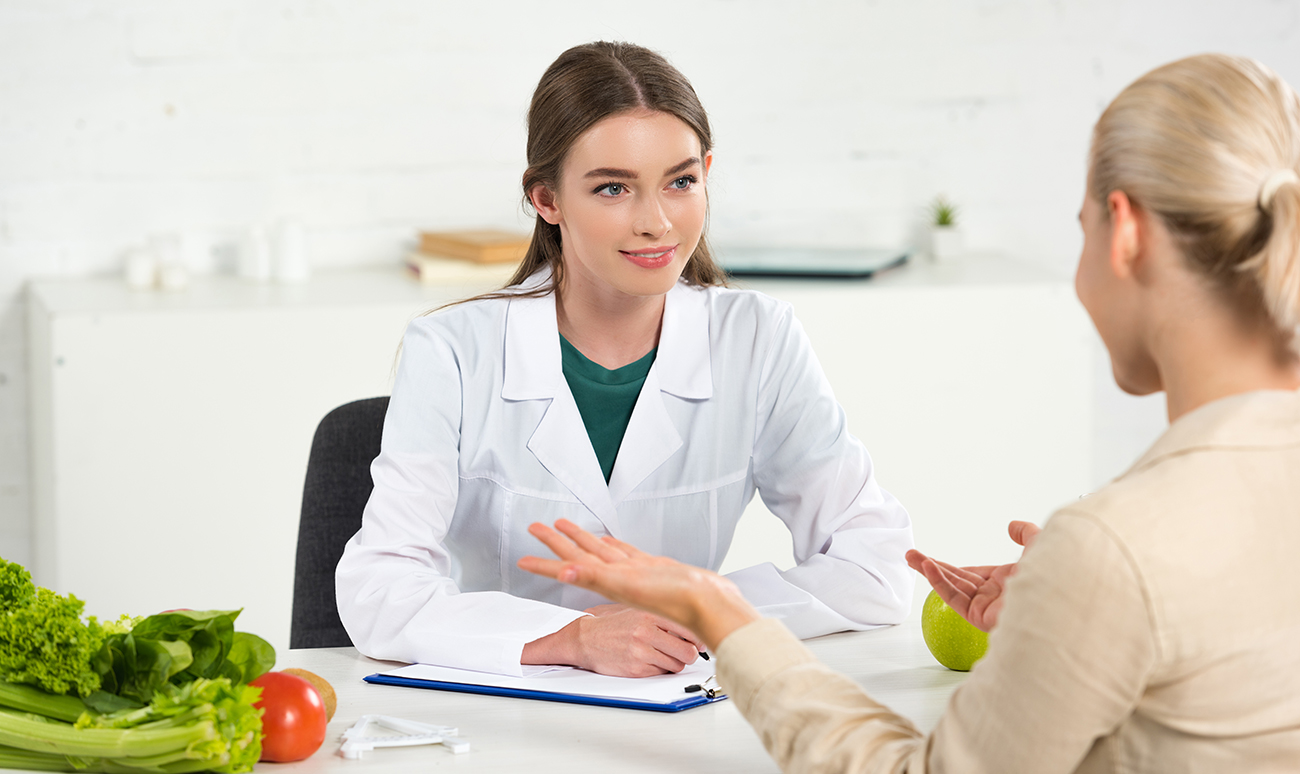 smiling dietitian in white coat looking at patient at table