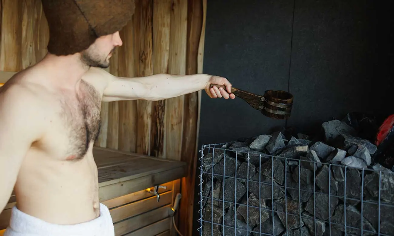 Man pouring water into stone in sauna room