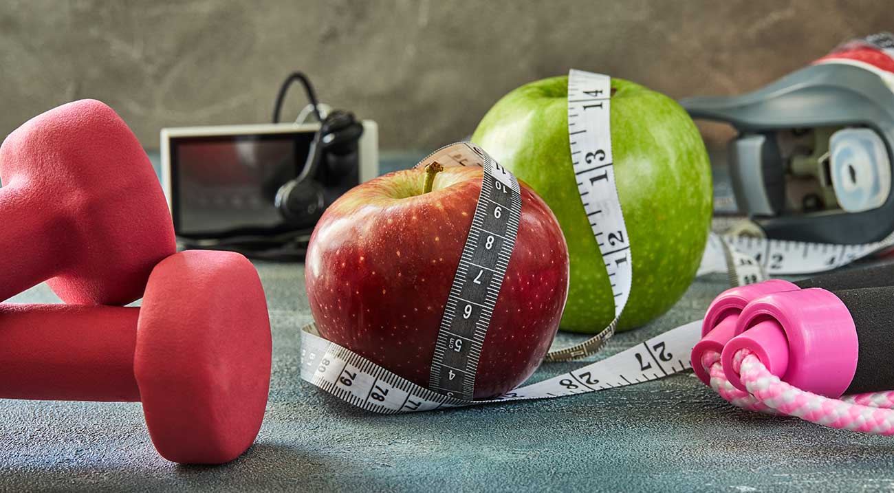 Dumbell, apple and waist measuring tape on a counter top